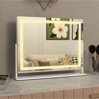 A lighted makeup mirror on a vanity table, with artwork and makeup brushes in the background.