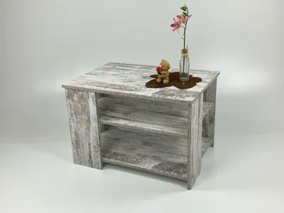 A small, rustic-style coffee table with shelves, decorated with a small teddy bear and a flower in a bottle.