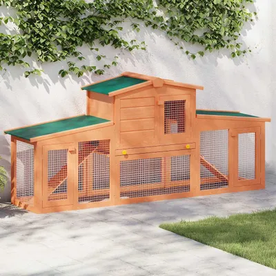 A wooden rabbit hutch with a green roof is shown outdoors on a paved patio, with ivy growing on a white wall in the background.