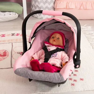 A doll is sitting in a pink and gray baby car seat on a rug.