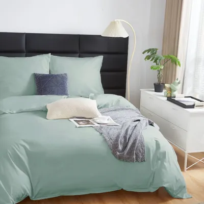 A neatly made bed with mint green bedding, pillows, and a throw blanket.