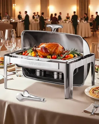 A chafing dish with a roasted turkey and vegetables is set on a table in a formal dining setting with people in the background.