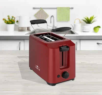 A red toaster sits on a wooden table in a kitchen setting.