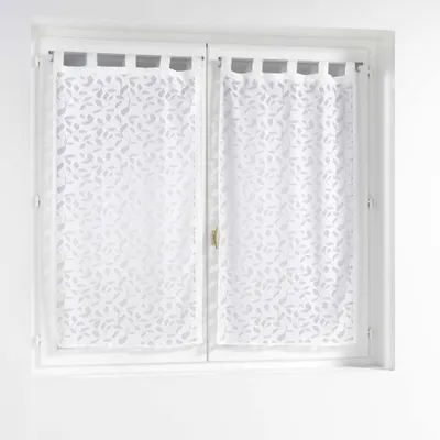 A window with two white sheer curtains with a leaf pattern.