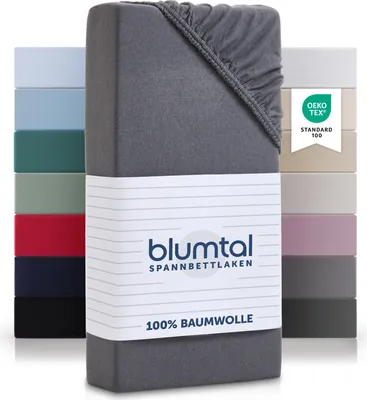 A stack of folded fitted sheets in various colors, with a close-up of one gray sheet in the foreground.