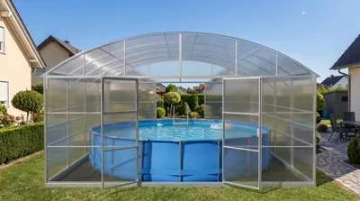 Zdjęcie produktu dla Pokrywa basenowa firmy Garten Dream. Wymiary: 5,5 x 12 metrów. Wykonana z poliwęglanu o grubości 10 mm. Przeznaczona do użytku przez cały rok. Odporna na śnieg i wiatr. Dwa drzwi po każdej stronie. Zabezpieczenie przed korozją.