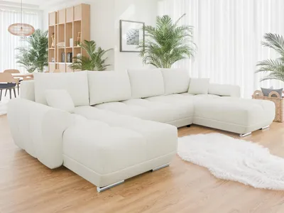 A white sectional sofa is shown in a well-lit living room with plants and wooden furniture in the background.