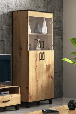 A tall, narrow wooden cabinet with glass doors and black handles, displayed in a modern living room setting.