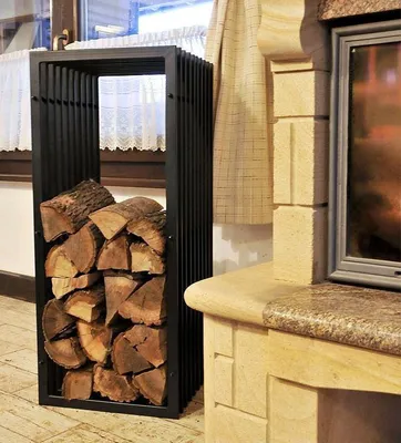 A black metal firewood rack filled with logs is placed next to a stone fireplace.