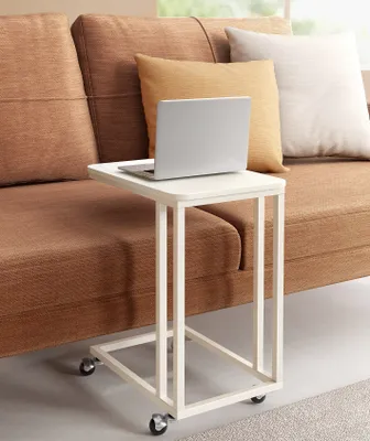 A white C-shaped side table with a laptop on it, placed next to a brown couch with pillows.