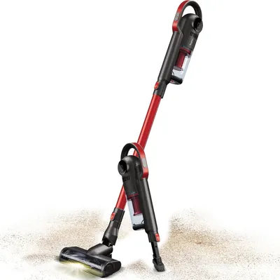 Two red and black cordless vacuum cleaners are shown leaning against each other on a light-colored surface with some dirt or dust.