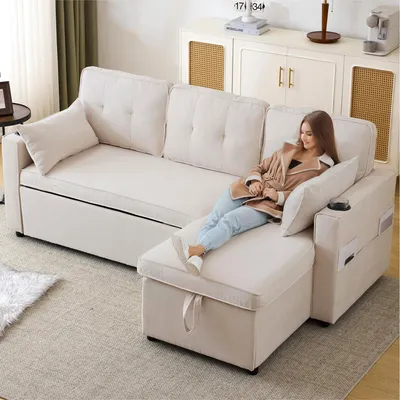 A woman is relaxing on a beige sectional sofa with a chaise lounge extension. The sofa is in a living room setting with a cabinet and curtains in the background.
