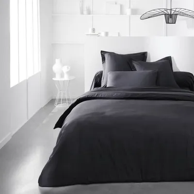 A neatly made bed with dark grey bedding in a minimalist bedroom setting.
