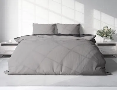 A neatly made bed with gray bedding in a bright room.