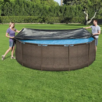 A man and a woman are putting a cover on an above-ground swimming pool in a grassy backyard.