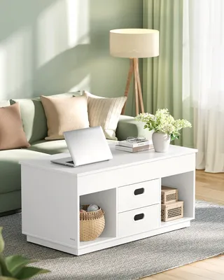 A white coffee table with a laptop, books, and a vase of flowers in a living room setting.