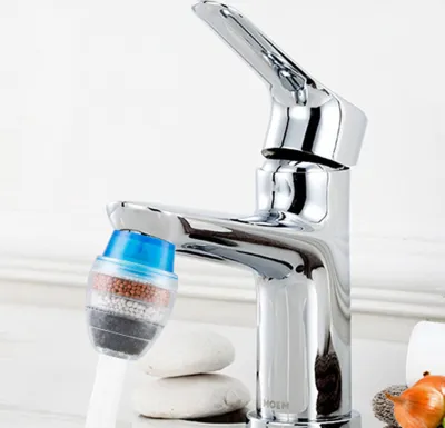 A close-up shot of a chrome faucet with a multi-layered water filter attached to the spout. Two smooth, light-colored stones are stacked beneath the faucet.