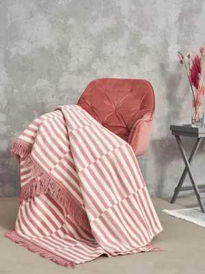 A pink velvet armchair with a striped throw blanket draped over it, next to a small side table with dried flowers.
