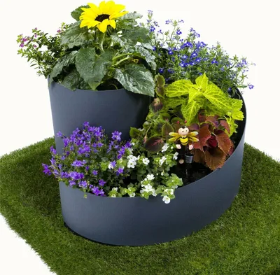 A multi-tiered planter filled with various flowers and plants, including a sunflower, set on a patch of artificial grass.