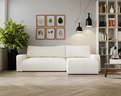 A white sectional sofa is displayed in a modern living room setting with artwork on the wall and a bookshelf in the background.