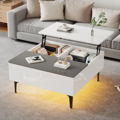 A modern living room scene featuring a multifunctional coffee table with its top lifted, revealing storage compartments. The table is placed in front of a sofa, with decorative items and books on display.