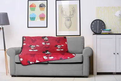 A red Mickey Mouse blanket is draped over a gray sofa in a living room setting.