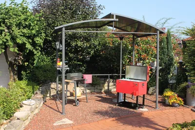 A backyard setting with a grill pavilion, grill, and cooler.