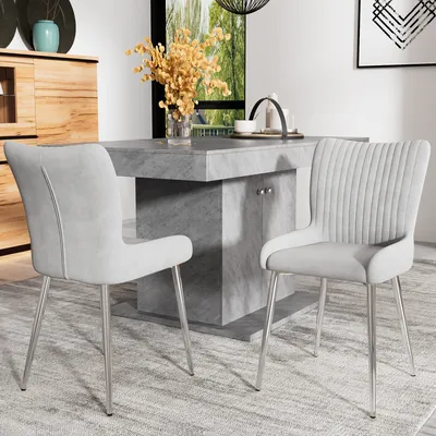 Two gray dining chairs with silver metal legs are placed in front of a gray dining table. A wooden cabinet is visible in the background.