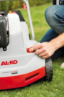 A person's hand is shown adjusting a red knob on a lawnmower.
