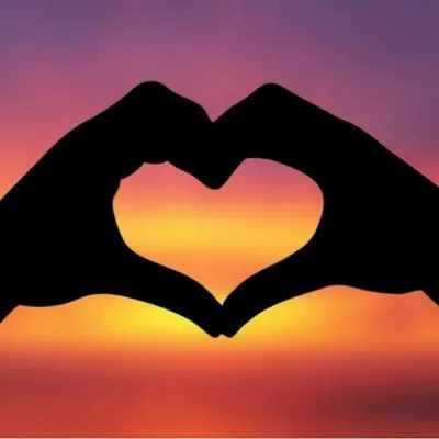 Silhouettes of hands forming a heart shape against a sunset.