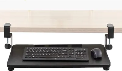 A black keyboard tray with a keyboard and mouse attached, clamped to the underside of a light-colored desk.