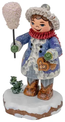 Holzfigur aus dem Erzgebirge: Lächelndes Winterkind mit grauer Pelzmütze, blauem Mantel, rotem Schal und braunen Stiefeln, haltend einen Lolli mit rosa Zuckerwerk und Lebkuchen, auf verschneiter Basis.