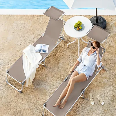 Two lounge chairs by a pool with a woman relaxing on one of them.