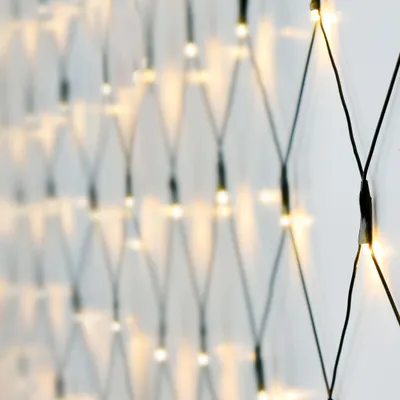 A close-up, angled view of a net of small, warm white LED lights against a white wall.