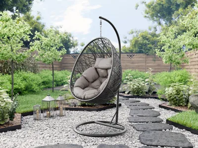 A hanging egg chair with cushions is placed in a garden setting with a stone pathway and lush greenery.