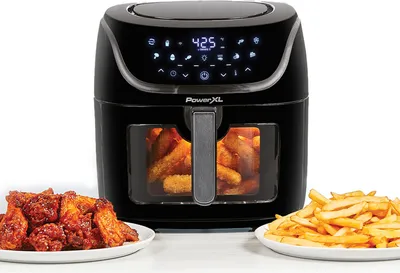 A black PowerXL Vortex PRO AirFryer XL is shown with plates of fried chicken wings and french fries in front of it. The air fryer has a digital display showing '425'.