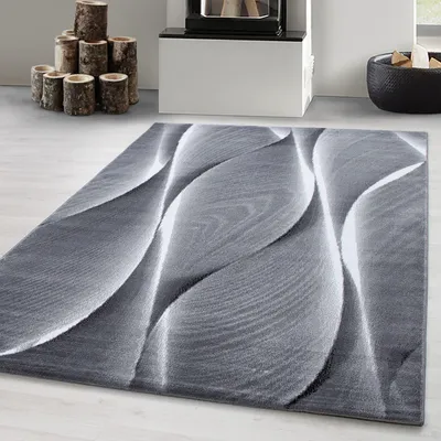 A modern abstract design rug with a grey and white wavy pattern is shown on a light wooden floor, with a fireplace and logs in the background.