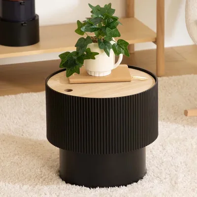 A small round side table with a plant on top, placed on a fluffy rug in a room.