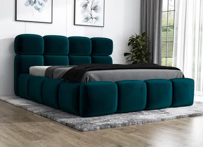 A dark green upholstered bed with a tufted headboard and frame, shown on a gray rug in a room with artwork on the wall and a plant near a window.