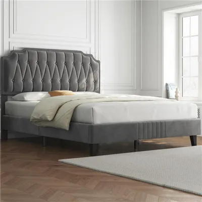 A dark gray upholstered bed with a tufted headboard is shown in a well-lit room with white walls and a large window.