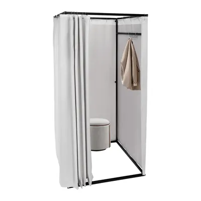 A freestanding changing room with white curtains, a beige jacket hanging on a rack, and a small round stool inside.