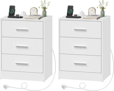 Two white bedside tables with three drawers each, placed side-by-side on a white background. Each table has a smartphone charging station and a small decorative vase with flowers on top.