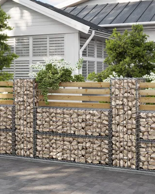 A gabion wall with wooden planks on top, in front of a house.