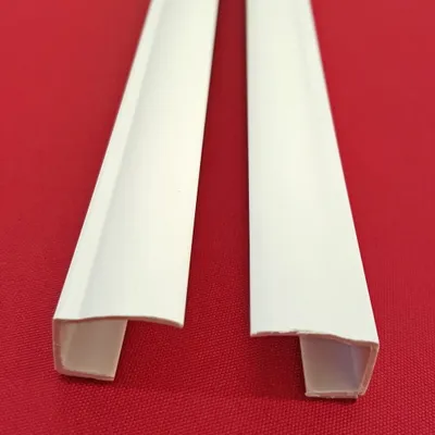 Two white PVC side rails for a roller blind are laid diagonally on a red background.