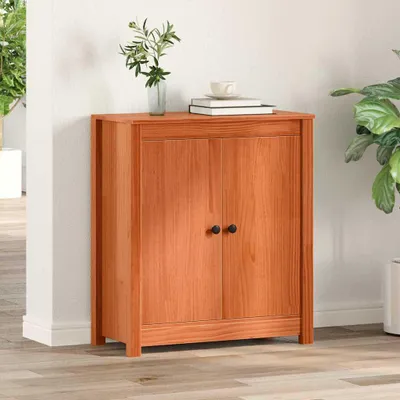 A wooden cabinet with two doors is placed against a white wall, with a plant and books on top.