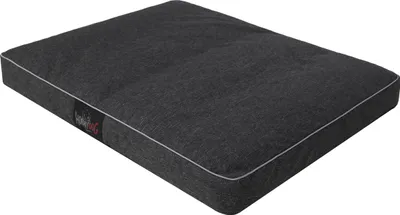 A dark gray dog bed with white piping, shown from a slightly elevated angle on a white background. A small black label with red and white text is visible on the left side of the bed.