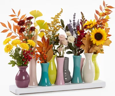 A collection of small, colorful ceramic vases filled with autumn-themed flowers and leaves.
