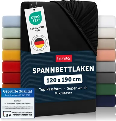 A black fitted sheet is shown, with a stack of other colored fitted sheets visible on the left and right sides. A tag with certifications and branding is attached to the sheet.