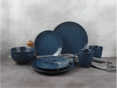 A dark blue stoneware dinnerware set is arranged on a gray surface against a textured gray background.