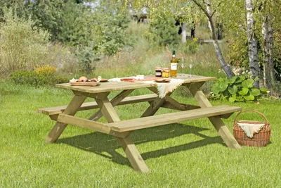 A wooden picnic table set up in a grassy outdoor area with trees and foliage in the background.